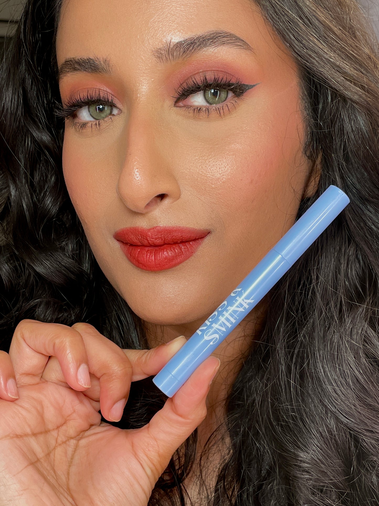 woman holding a brick red lip crayon from kiss and smink beauty brand 